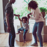 Young family playing inside a home. There are cardboard boxes behind them. 