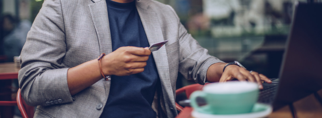 Close up of a man's hands. One is holding a credit card while the other is using a laptop.