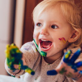 Toddler with paint all over their hands and face.
