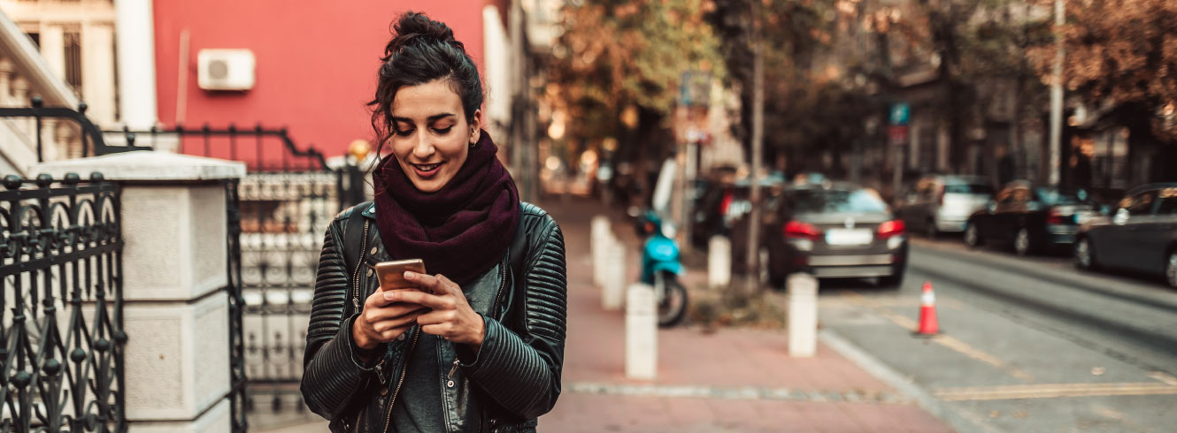 A young woman walking down a sidewalk looking down at her phone.