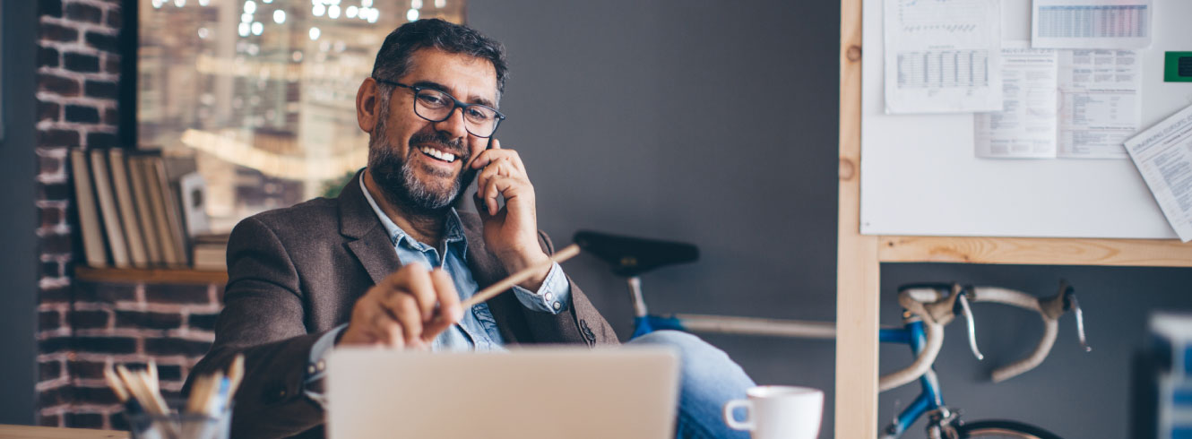 A businessman talking on the phone while looking at a laptop.