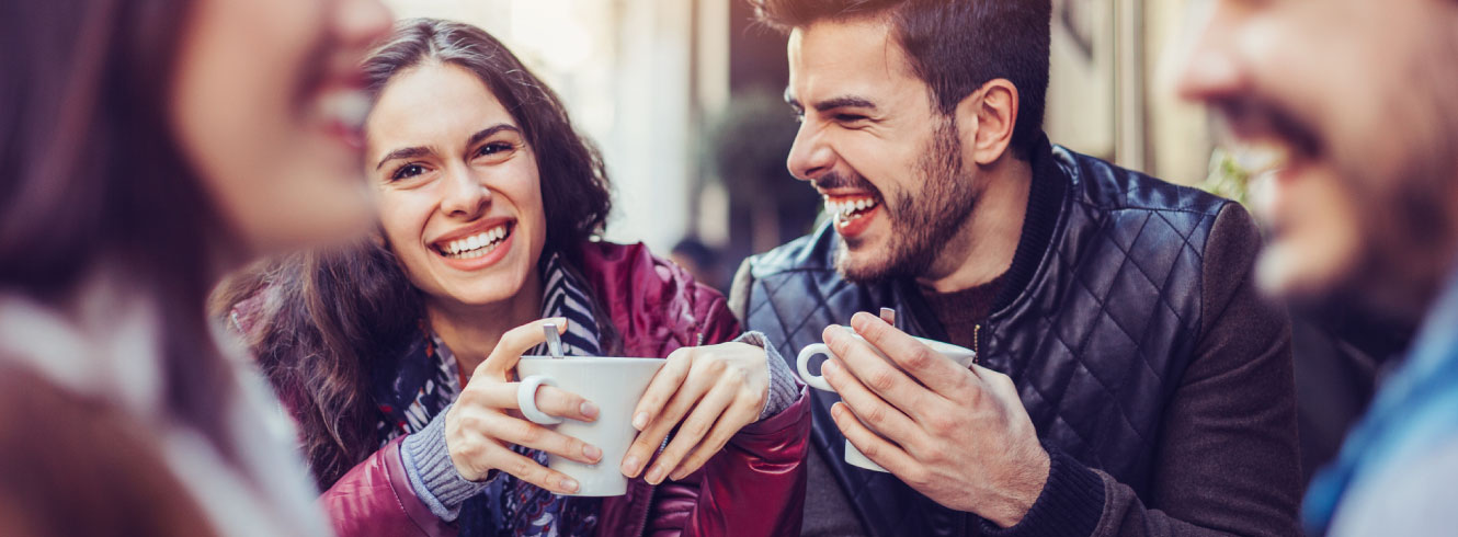 Group of friends laughing outside drinking coffee.