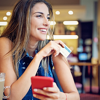 Young woman holding a credit card in one hand and her phone in the other.